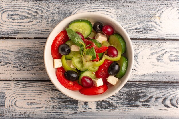 Draufsicht frischer Gemüsesalat mit geschnittenen Gurkentomaten-Oliven- und Weißkäse-Innenplatte auf der grauen Schreibtischgemüsesalat-Mahlzeit Mahlzeitfarbe