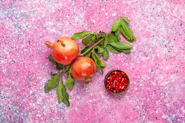 Draufsicht frischer Granatapfel mit grünen Blättern auf rosa Oberfläche