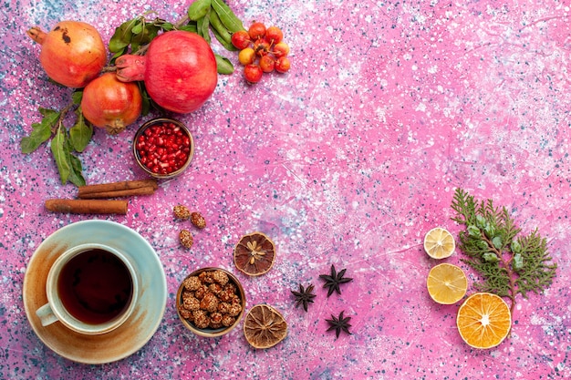 Draufsicht frischer Granatapfel mit grünen Blättern und Tasse Tee auf der rosa Oberfläche