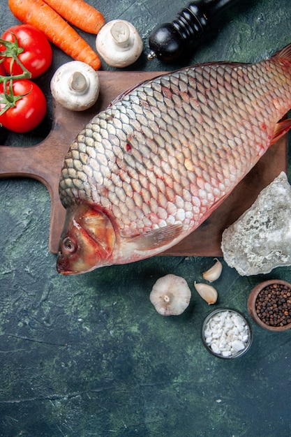 Draufsicht frischer roher Fisch auf Schneidebrett mit Tomaten dunkelblauem Hintergrund