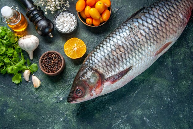 Draufsicht frischer roher Fisch mit Kumquats und Grüns auf dunklem Hintergrund