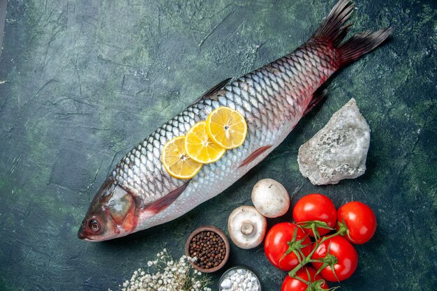 Draufsicht frischer roher Fisch mit Tomaten und Zitrone auf dunkelblauem Hintergrund