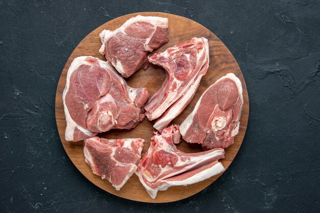 Draufsicht frisches Fleisch schneidet rohes Fleisch auf rundem Holztisch auf dunkler Lebensmittelfrische Tierkuhmehlküche