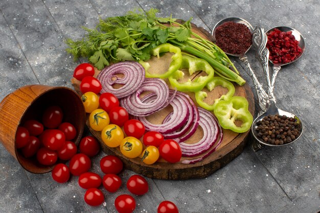 Draufsicht frisches Gemüse in Scheiben geschnitten und ganz wie Zwiebeln grüne Paprika rote und gelbe Tomaten auf dem braunen Schreibtisch und grau