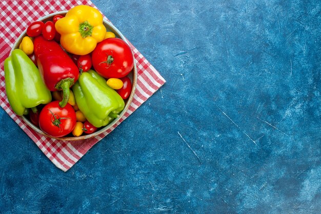 Draufsicht frisches Gemüse Kirschtomaten verschiedene Farben Paprika Tomaten cumcuat auf Platte auf rot weiß kariertem Küchentuch auf blauem Tisch mit Kopienraum