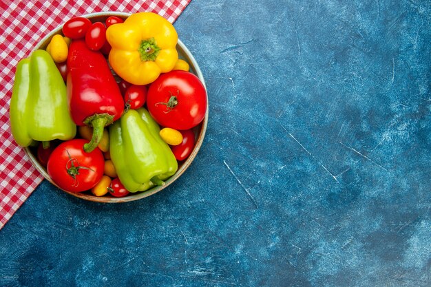 Draufsicht frisches Gemüse Kirschtomaten verschiedene Farben Paprika Tomaten cumcuat in Schüssel auf rot und weiß karierten Tischdecke auf blauem Tisch mit Kopie Platz