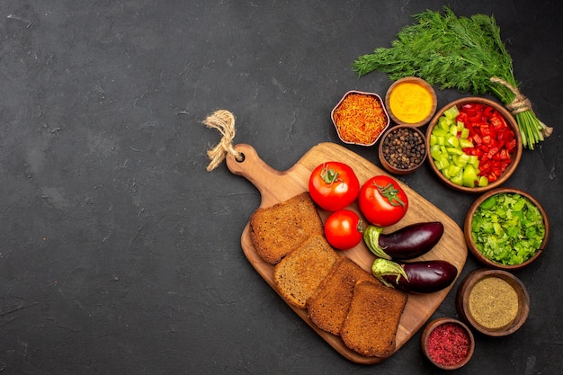 Draufsicht frisches Gemüse mit dunklen Brotlaiben und Gewürzen auf der dunklen Oberfläche Salatmahlzeit Brotessen