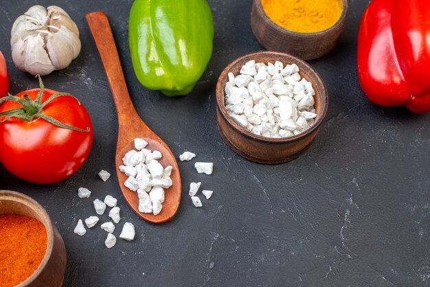 Draufsicht frisches Gemüse Tomaten Knoblauch farbige Paprika Meersalz in Holzlöffel Gewürze in Schalen auf schwarzem Tisch