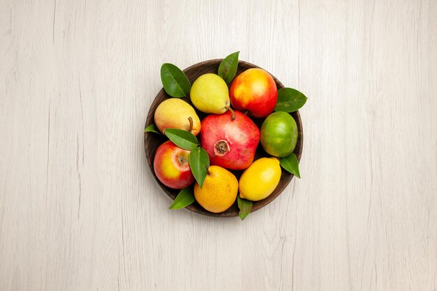 Draufsicht frisches Obst Äpfel Birnen und andere Früchte im Teller auf weißem Schreibtisch Obst reife Baumfarbe milde viele frische