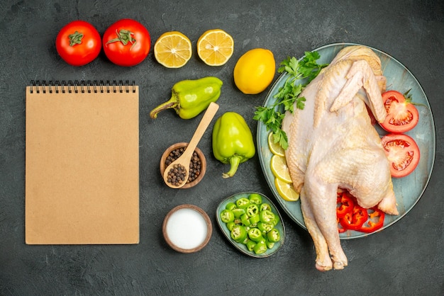 Draufsicht frisches rohes Hühnchen mit Tomaten, Zitrone und Grün auf dunklem Hintergrund