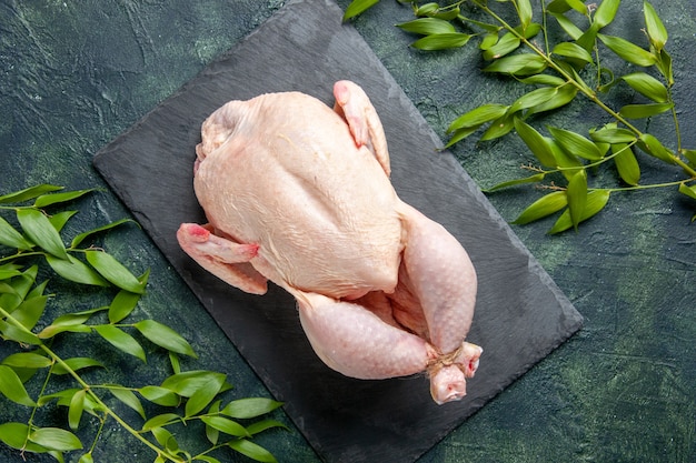 Draufsicht frisches rohes Huhn mit grünen Blättern auf dunklem Hintergrund Hühnermehl Tierfleisch Foto Lebensmittelfarbe Küche