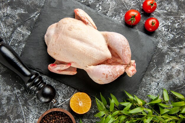 Draufsicht frisches rohes Huhn mit Tomaten auf hell-dunklem Hintergrund Küchenmahlzeit Tierfoto Huhn Farbe Bauernhoflebensmittel