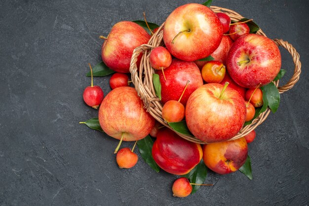 Draufsicht Früchte rot-gelbe Kirschen und Äpfel mit Blättern im Korb