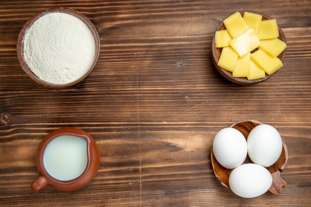 Draufsicht ganze rohe Eier mit Käsemehl und Milch auf den braunen Holztischprodukten Eiteiggebäck