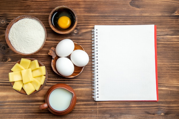 Draufsicht ganze rohe Eier mit Mehlmilch und Käse auf braunen Tischeierteigmehlstaubprodukten