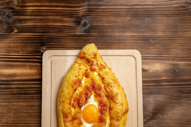 Draufsicht gebackenes Brot mit gekochtem Ei auf hölzerner Oberfläche Brötchenfutter-Ei-Frühstücksteig