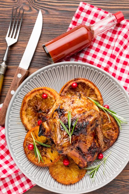 Draufsicht gebackenes Huhn und Orangenscheiben auf Teller mit Besteck und Soße