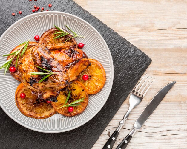 Draufsicht gebackenes Huhn und Orangenscheiben auf Teller mit Besteck