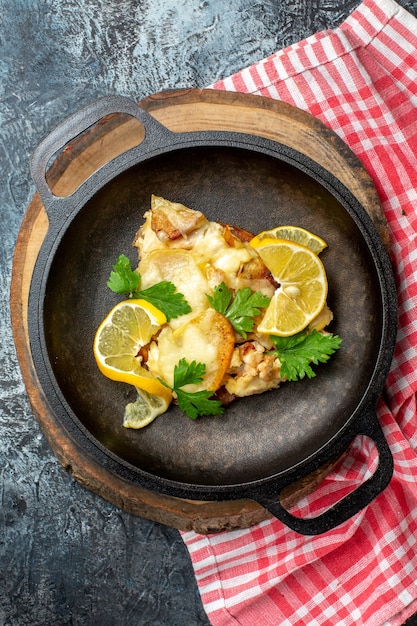 Draufsicht gebratener Fisch in Pfanne auf Holzbrett auf grauem Hintergrund