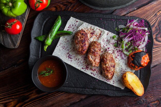 Draufsicht gebratenes Fleisch mit Bratkartoffeln und Tomaten und Zwiebeln und würziger Sauce in dunkler Platte