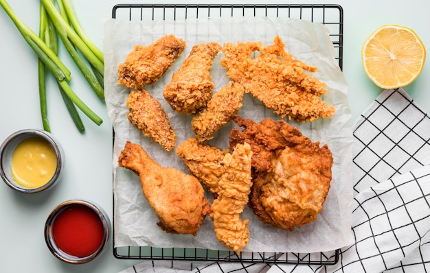 Draufsicht gebratenes Huhn auf Tablett mit Saucen, Frühlingszwiebeln und Zitrone