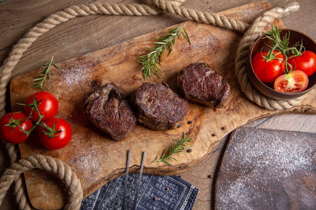 Draufsicht gebratenes leckeres Fleisch mit frischen roten Tomaten und Grüns auf dem hölzernen Schreibtischmahlzeitnahrungsmittelessen-Fleischfoto