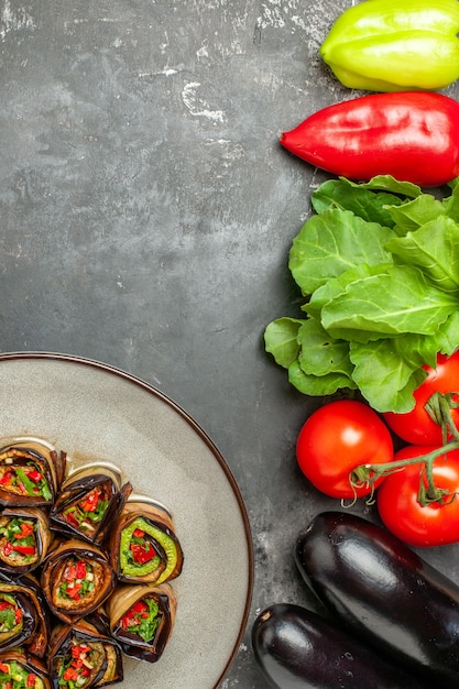 Draufsicht gefüllte Auberginenröllchen in weißem Teller Tomaten Paprika Auberginengrün auf grauer Oberfläche