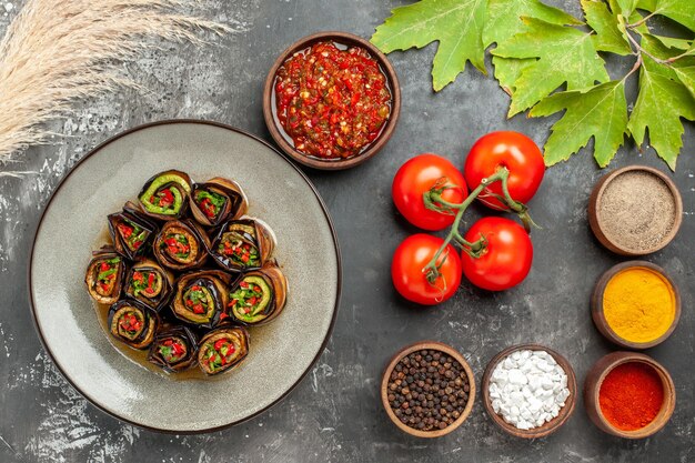 Draufsicht gefüllte Auberginenrollen verschiedene Gewürze adjika in kleinen Schüsseln und Tomaten auf grauer Oberfläche