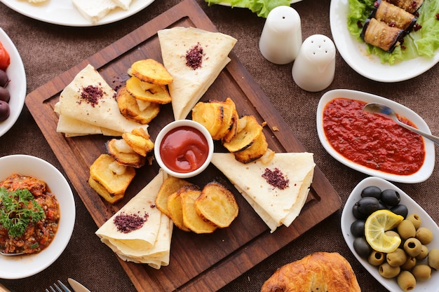 Draufsicht gegrillte Kartoffel mit Ketchup-Schwarz-Grün-Olivenbrot-Auberginen-Roulette-geröstetem Gemüsesalat Salz und Pfeffer auf dem tablejpg