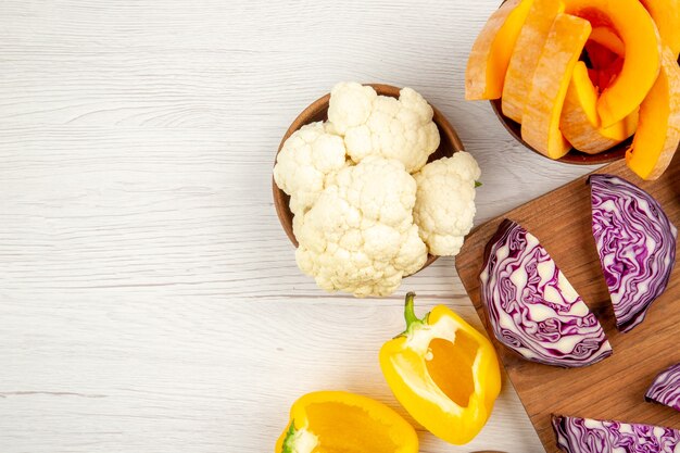 Draufsicht gehackter Rotkohl auf Holzbrett geschnittenen gelben Paprika Blumenkohl geschnittenen Kürbis in Schalen auf weißem Tisch freien Platz