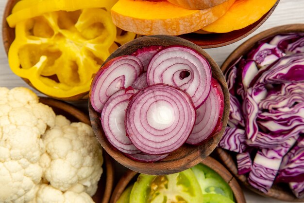 Draufsicht gehacktes Gemüse geschnittener Rotkohl geschnittener Kürbis geschnittener gelber Paprika geschnittener Zwiebelschnitt grüner Tomatenblumenkohl in Schalen auf weißem Tisch