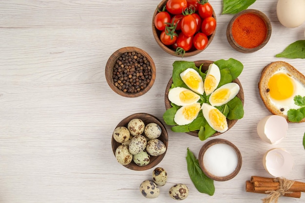 Draufsicht gekochte Eier mit Tomaten und Gewürzen auf hellem Hintergrund Foto Morgenmahlzeit Mittagessen Farbe Essen Salat Frühstück