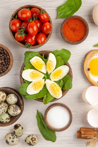 Draufsicht gekochte Eier mit Tomaten und Gewürzen auf weißem Hintergrund Fotos Morgenmahlzeit Frühstück Mittagessen Farbsalat