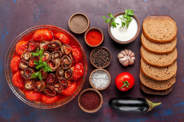 Draufsicht gekochte Gemüsemahlzeit Tomaten und Auberginen mit Gewürzen und Brot auf dunklem Schreibtisch