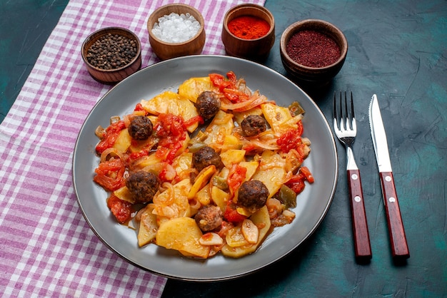 Draufsicht gekochte geschnittene Kartoffeln mit Fleischbällchen zusammen mit Gewürzen auf dem dunkelblauen Hintergrund.