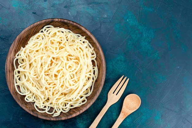 Draufsicht gekochte italienische Nudeln innerhalb der runden hölzernen Platte auf dem blauen Schreibtischnudeln Italien Essen Abendessen Teig Fleisch