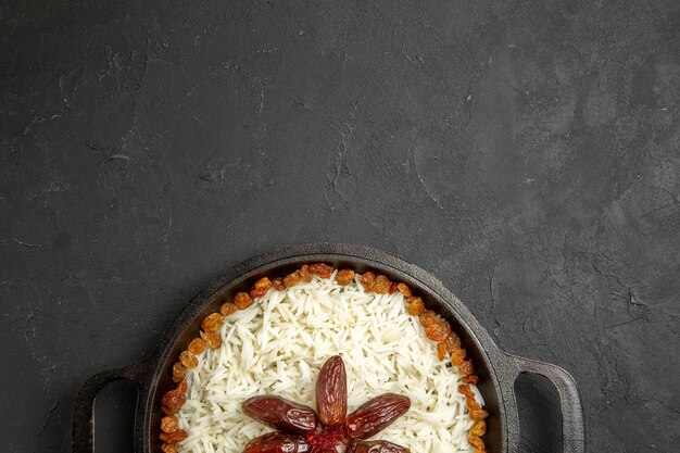 Draufsicht gekochter Reis mit Rosinen in der Pfanne auf dunkler Oberfläche Reis östliches Essen Abendessen