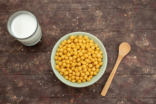 Draufsicht gelbe Müsli innerhalb Platte mit frischer kalter Milch und Löffel auf dunklem Frühstück Cornflakes Müsli Essen