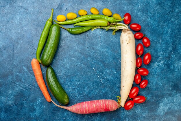 Draufsicht Gemüse Gurke Cumcuat Karotte Kirschtomaten rosa und weißer Rettich grüne Peperoni auf blauem Hintergrund