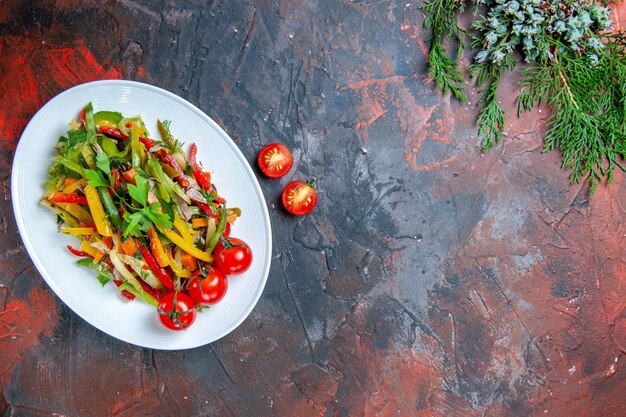 Draufsicht Gemüsesalat auf ovalem Teller Kirschtomaten auf dunkelrotem Tisch freien Platz