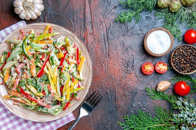 Draufsicht Gemüsesalat auf Teller auf Tischtuchgabel Salz und schwarzen Pfeffer Knoblauch Tomaten auf dunkelrotem Tisch