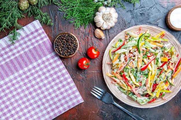 Draufsicht Gemüsesalat auf Teller auf Tischtuchgabel Salz und schwarzen Pfeffer Knoblauch Tomaten auf dunkelrotem Tisch