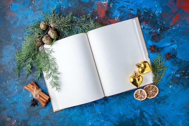 Kostenloses Foto draufsicht geöffnet notebook tannenzweige kegel weihnachtsbaum spielzeug auf blauer oberfläche