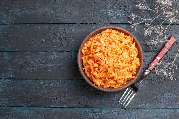 Draufsicht geriebener Karottensalat in brauner Platte auf dem dunkelblauen rustikalen Schreibtisch Gesundheit Salat reife Gemüsediätfarbe