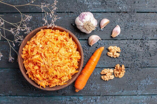 Draufsicht geriebener Karottensalat mit Knoblauch im Teller auf dunkelblauem rustikalem Schreibtisch Gesundheit Salat reifes Gemüse Farbdiät