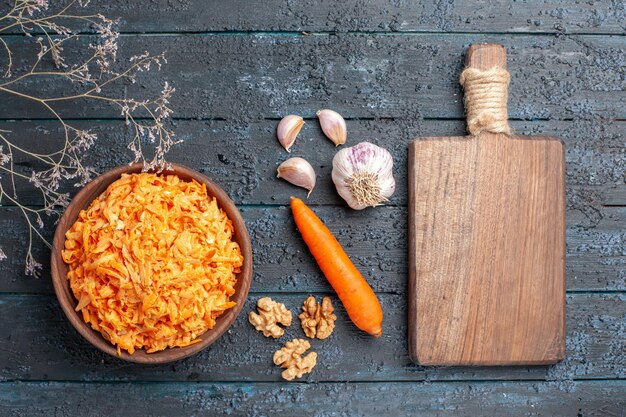 Draufsicht geriebener Karottensalat mit Knoblauch innerhalb des Tellers auf dem dunkelblauen rustikalen Schreibtischgesundheitssalat reife Gemüsefarbdiät