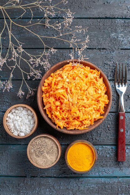 Draufsicht geriebener Karottensalat mit Knoblauch und Gewürzen auf dem dunkelblauen rustikalen Schreibtisch Gesundheit Farbsalat reife Gemüsediät