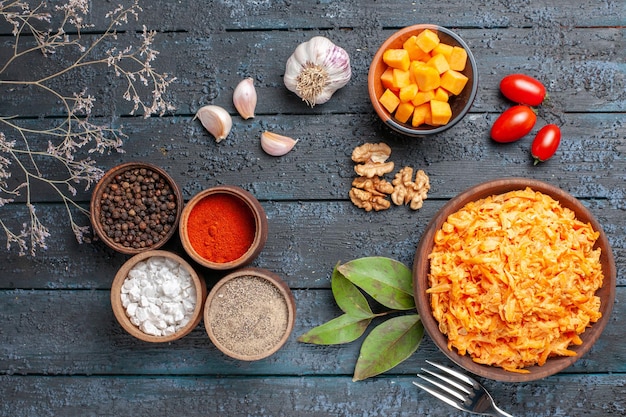 Draufsicht geriebener Karottensalat mit Knoblauchwalnüssen und Gewürzen auf dem dunklen Schreibtisch Gesundheitsdiät orangefarbener reifer Salat