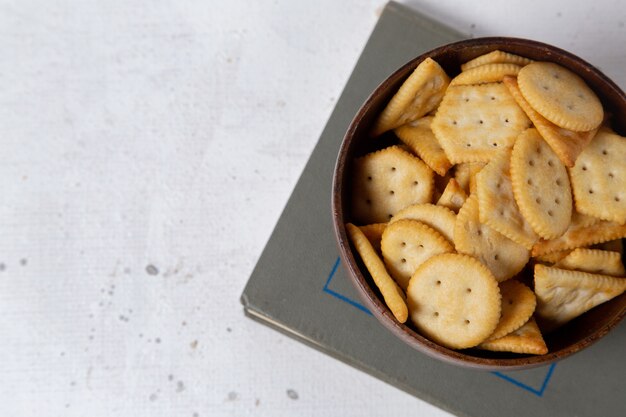 Draufsicht gesalzene Cracker innerhalb der braunen Platte auf dem knackigen Snackfoto des hellen Hintergrundcrackers