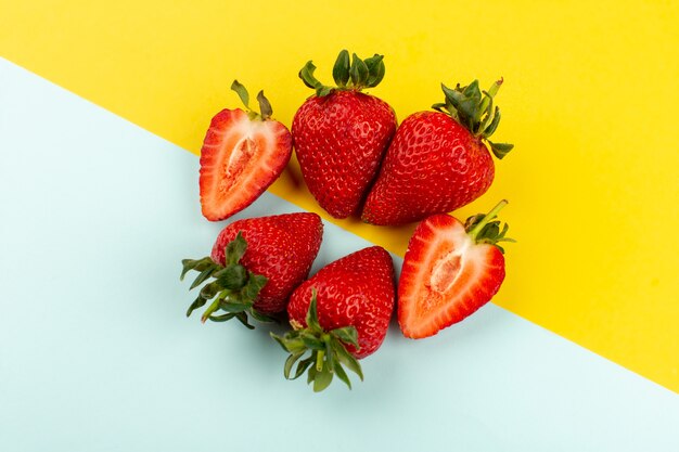 Draufsicht geschnittene ganze Erdbeeren saftig weich auf dem blau-gelben Boden